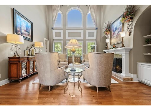 Elegant living room with two chairs by a glass table before arched windows and a fireplace.